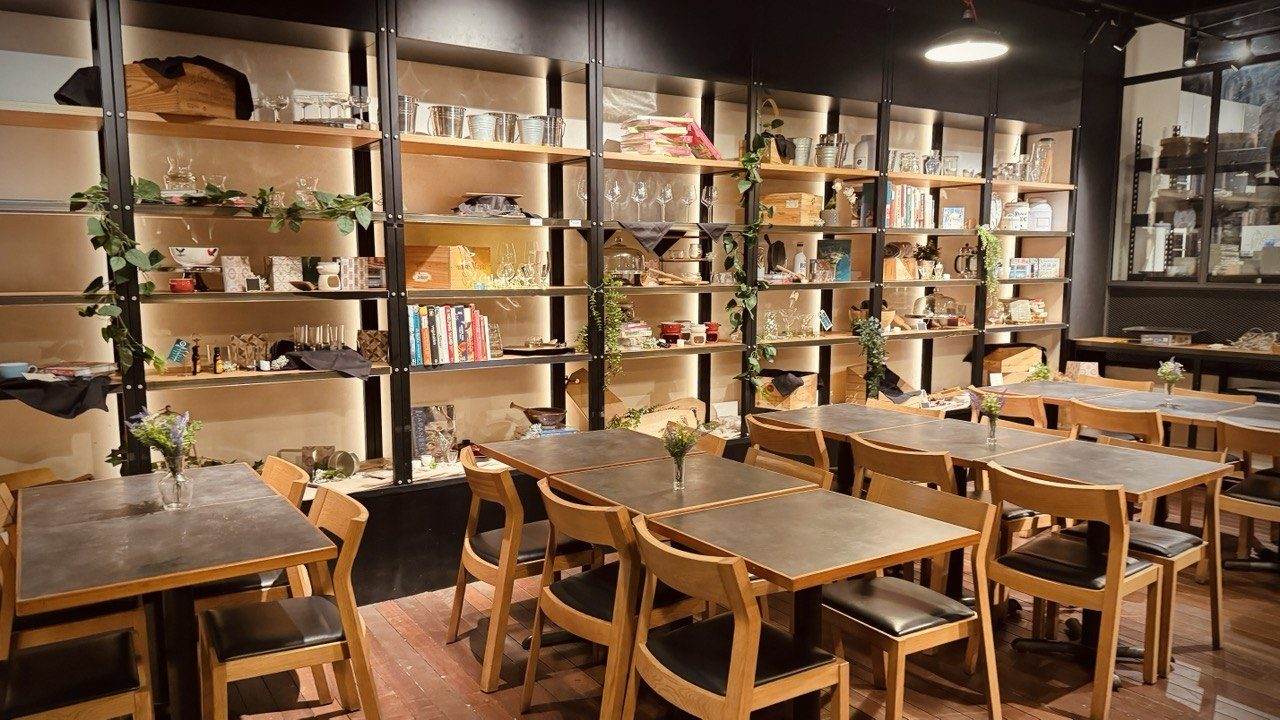 The dedicated dining area at D'Open Kitchen Singapore, with wooden tables, chairs and shelves of glassware and cookbooks