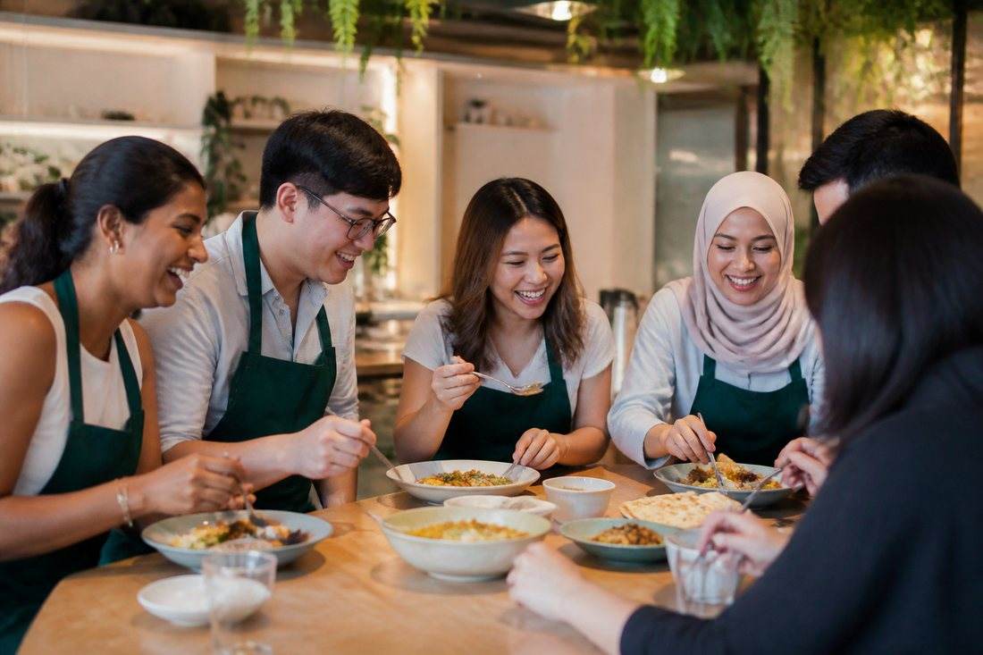 A diverse Singapore team including a hijab-wearing colleague sharing a halal meal they cooked together