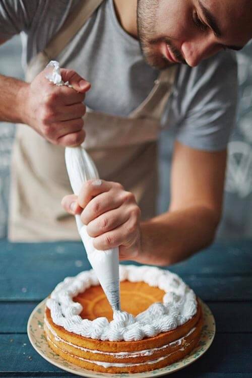 man putting cream on cake in baking class